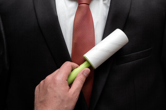 Business man cleaning his suit with adhesive lint roller. Dry cleaning with  sticky brush for cleaning clothes.