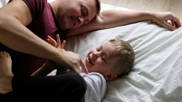 Happy father and son having fun on a bed, laughing. View from above