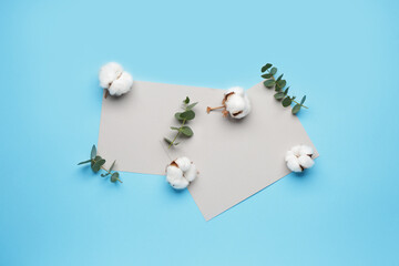 Blank cards, beautiful cotton flowers and eucalyptus leaves on color background