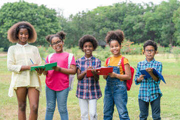 Portrait of African American childrens holding books and looking at camera while standing in park of school