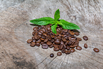 Coffee beans and mint leaves on a wooden surface.