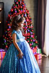 Fototapeta premium girl with dark hair standing on a box with gifts. Christmas tree in the background. smiles