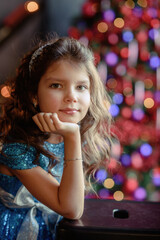 girl with dark hair standing on a box with gifts. Christmas tree in the background. smiles