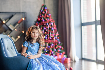 girl with dark hair standing on a box with gifts. Christmas tree in the background. smiles