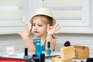 Fototapeta na wymiar little girl put on funny mother's makeup and does manicure