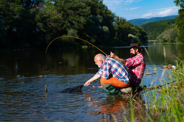 Angler catching the fish. Senior man fishing. Bearded brutal hipsters fishing. Men relaxing nature background. Against the background of the water with a reflection of the forest. Fishing.