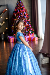 girl with dark hair standing on a box with gifts. Christmas tree in the background. smiles