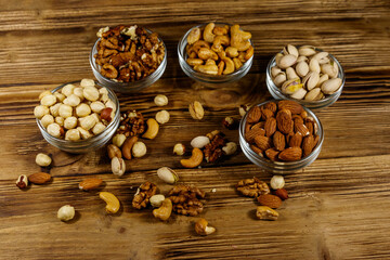 Fototapeta premium Assortment of nuts on wooden table. Almond, hazelnut, pistachio, walnut and cashew in glass bowls. Healthy eating concept