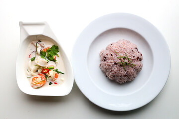 Close up Seafood Coconut Soup served in a boat shaped white bowl With riceberry Put on the white table Ready to eat Taken from above
