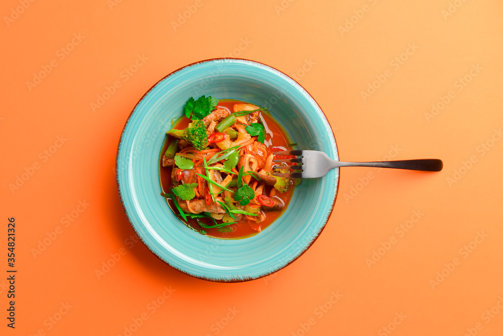 Wall mural meat salad with vegetable and fresh greenery served in a bowl isolated on bright orange background.