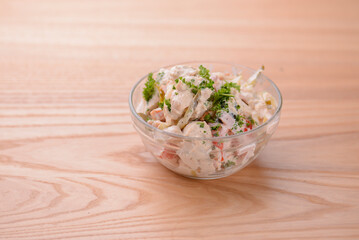 Vegetable salad with green peas, herbs, meat and mushrooms in a glass bowl on light wooden table. Healthy diet.