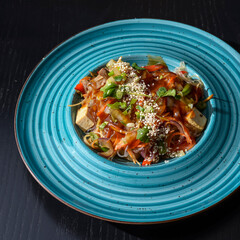 Plate of Traditional Asian salad served in a blue plate at a restaurant over black wooden table.