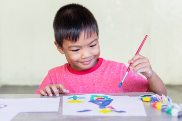 Portrait image of 5-6 yeas old child boy. Asian student drawing and painting colours on the paper in the room. Study​ from​ home, social​ Distance, Kid and education concept.