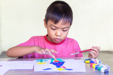 Portrait image of 5-6 yeas old child boy. Asian student drawing and painting colours on the paper in the room. Study​ from​ home, social​ Distance, Kid and education concept.