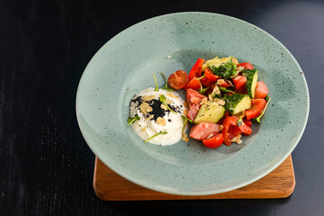 Fresh vegetables and green salad served in a blue plate over black rustic wooden table.