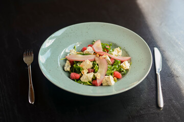 Fresh vegetables and green fruit salad served in a blue plate over black rustic wooden table.
