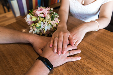Obraz na płótnie Canvas A man and a woman hold hands in a cafe, next to a bride’s bouquet, shot in the middle view in natural light.
