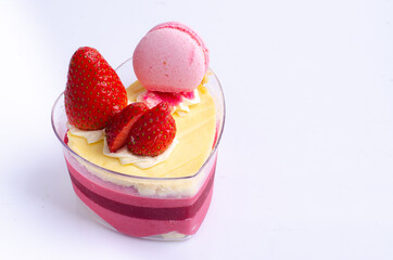 Heart shaped red velvet cake decorated with strawberry and macaron on pink background