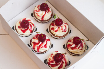 Vanilla cupcakes in gift box with berry sauce, whipped cream and fresh cherries on top.