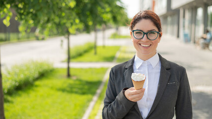 Business woman walks down the street and enjoys ice-cream. Happy girl in a suit eats an ice cream cone on a hot sunny summer day. Lunch break of an office employee.