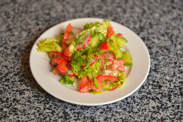 Vegetable salad with radishes,cucumber, sweet pepper and dill. Served in a white plate over grey textured table.