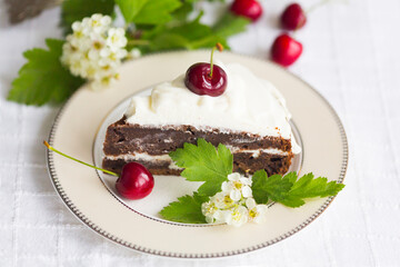 Piece of homemade cherry cake with whipping cream and cherry berry on top surrounded with flowering  branches on white tablecloth