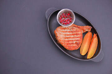 Rib eye steak served with baked potatoes and cranberry sauce on a black tray over black background.