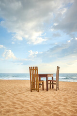Wooden table and two chairs on a beach.