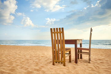 Wooden table and two chairs on a beach.