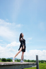Asian sexy woman and long hair in black dress smiling and standing on wooden bridge in natural sunlight with blue sky and wind in summer season on the mountain