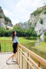 Asian sexy woman and long hair in black dress and jean jacket smiling and standing on concrete bridge near rocky mountain, river and lake in natural sunlight and wind on summer season in the park.