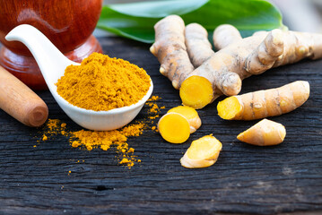 fresh turmeric root and turmeric powder in spoon on wooden background
