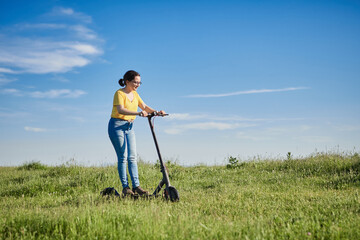 young woman with a scooter across the field and blue sky