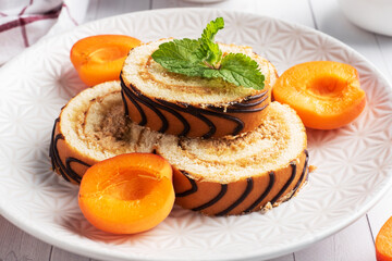 Pieces of sweet roll with cream filling on a plate. Fresh apricot berries and mint leaves.