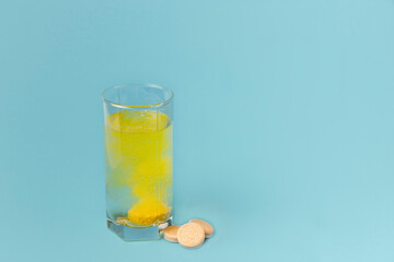 A glass of water and pills on a blue background close-up. A tablet of vitamins is dissolved in water. Copy space.