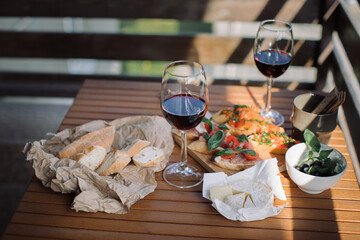 Red wine, brushettas with vegetables, salami and basil, black olives, bread and cheese on wooden table on summer terrace. Home party concept.