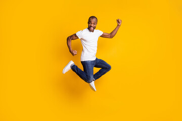 Fototapeta na wymiar Full size photo of cheerful delighted afro american guy jump celebrate discount spring time win raise fists scream yes wear denim jeans white isolated over shine color background