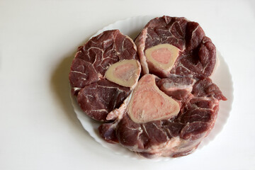A piece of raw beef drumstick with bone and bone marrow. The meat for boiling boulen is on a white...