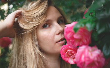 Fototapeta premium blond woman smiling in a flowering bush of pink roses
