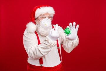 Fototapeta na wymiar Fuck you covid. Photo of old bearded santa hold flu bacteria holly atmosphere save winter holidays show middle finger wear plastic goggles mask hat shirt suspenders isolated red background