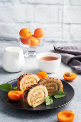 Pieces of sweet roll with cream filling on a plate. Fresh apricot berries and mint leaves.
