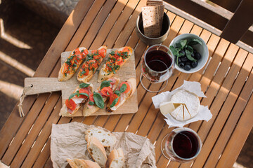 Tomato and salami bruschettas with red wine on wooden table on summer terrace. Home party concept.