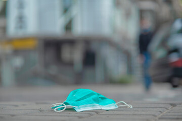 Discarded medical face mask lies on the sidewalk. Face masks polluting streets of the city since Coronavirus COVID-19. Soft focus.
