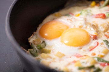 In a black pan, appetizer omelet fried eggs with fresh vegetables.