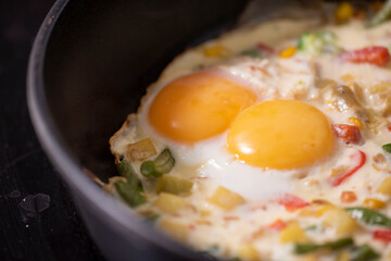 In a black pan, appetizer omelet fried eggs with fresh vegetables.