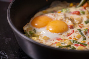 In a black pan, appetizer omelet fried eggs with fresh vegetables.