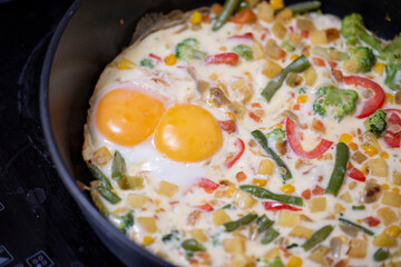 In a black pan, appetizer omelet fried eggs with fresh vegetables.