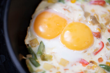 In a black pan, appetizer omelet fried eggs with fresh vegetables.