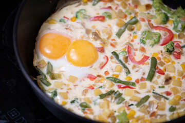 In a black pan, appetizer omelet fried eggs with fresh vegetables.