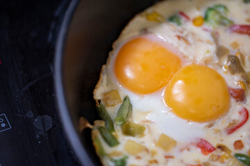 In a black pan, appetizer omelet fried eggs with fresh vegetables.